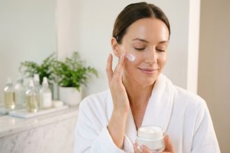 Femme appliquant une crème hydratante au panthénol sur son visage dans une salle de bain minimaliste